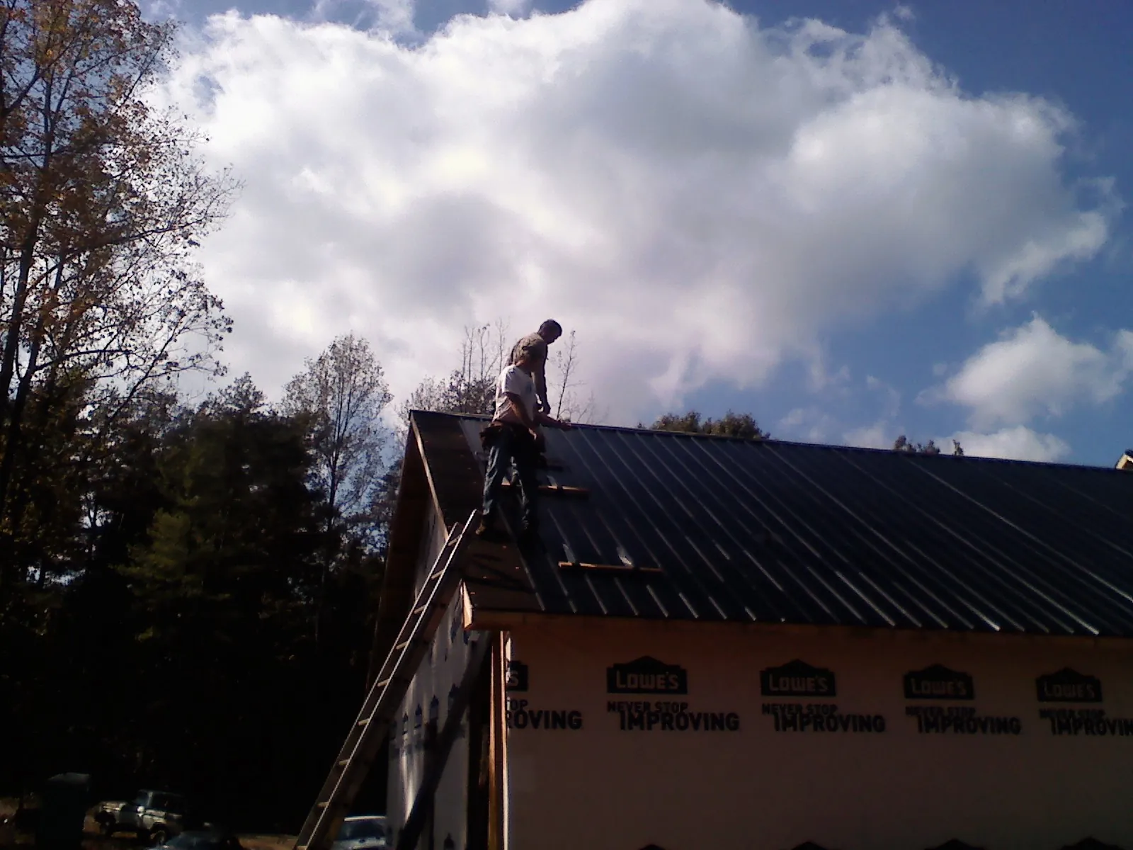 Roofer fastening dark metal panels high against a cloudy sky, from a Roof Inspection job in Turtle Creek